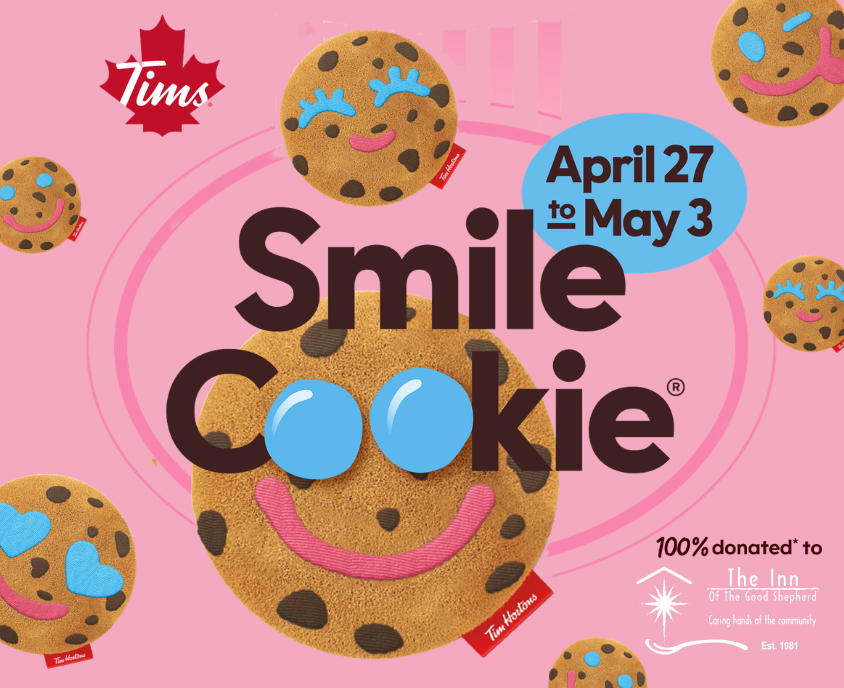 Pink promotional graphic for the Tim Hortons Smile Cookie campaign featuring a large plush Smile Cookie in the center with smaller plush cookies around the border. Campaign runs April 27 to May 3. Text states that 100% donated to The Inn of the Good Shepherd.