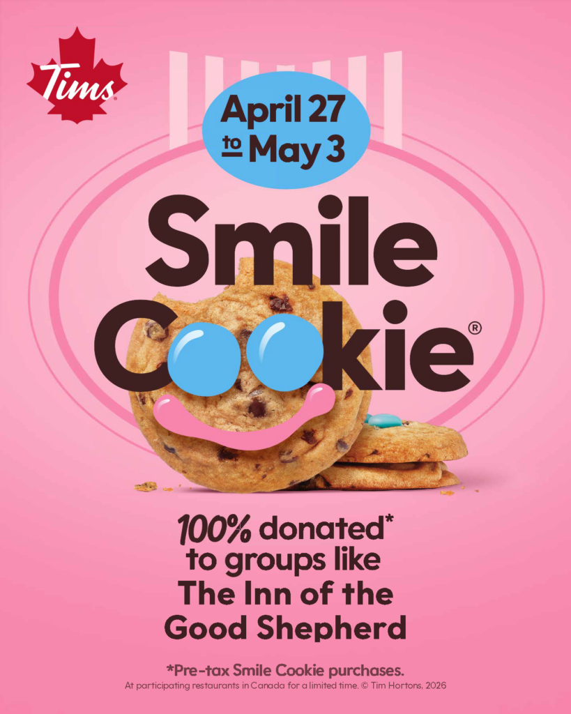 Pink promotional poster for the Tim Hortons Smile Cookie campaign. Features a chocolate chip Smile Cookie with blue icing eyes and a pink smile. Campaign runs April 27 to May 3. Text states that 100% of pre-tax Smile Cookie purchases are donated to groups like The Inn of the Good Shepherd.